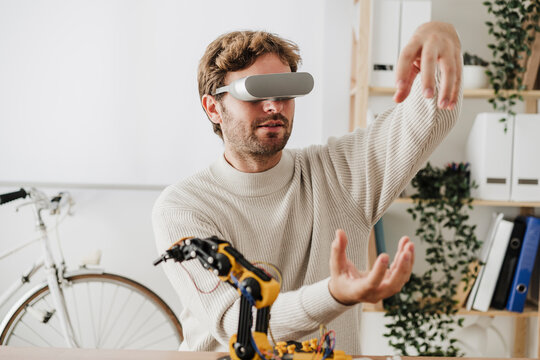 Engineer with futuristic goggles working on model of robotic arm in workplace