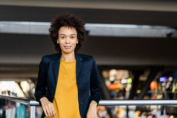 Smiling businesswoman wearing blazer leaning on railing