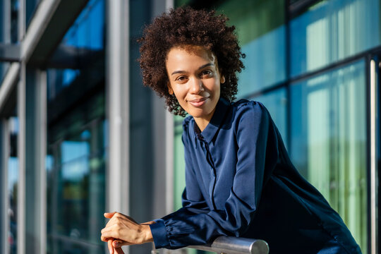 Smiling businesswoman with curly hair leaning on railing