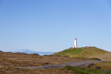 Fototapeta na wymiar Lighthouse atop a green hill in Iceland under a clear pale blue sky on a sunny day
