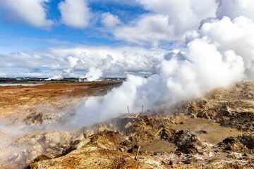 Hot spring in Iceland with steam rising from it and merging into the huge fluffy white clouds
