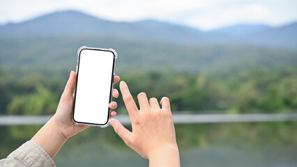 Young Asian female using her modern smartphone to take a picture of lake and mountain