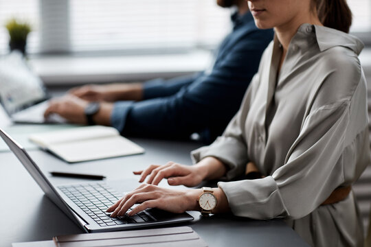 Young businesswoman or student in grey silk dress typing on laptop keyboard while looking for online data or carrying out task
