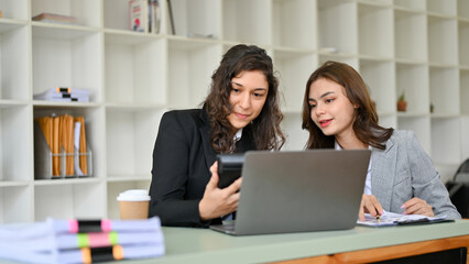 Two Caucasian businesswomen are cooperating, working on a business report together.