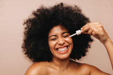 Beautiful young woman applying cosmetic oil on her face