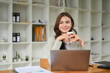 Obraz premium Charming caucasian businesswoman at her desk, holding a coffee cup, looking away