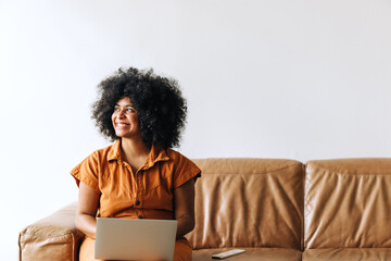 Thoughtful ethnic businesswoman smiling while working on a laptop