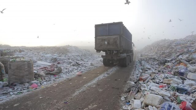 A dirty garbage truck pulls into a large city waste dump.