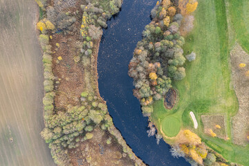 Aerial view on multicolored trees in autumn, and green grass, forest, wild nature, river, contrasts. Beautiful autumn in the village. Golf course. 