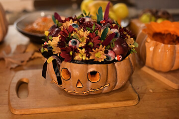 Halloween pumpkin decorated with flowers and gummy eyes on a wooden table. Conceptual still life of Halloween.