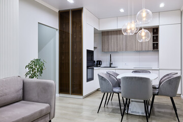 Modern kitchen interior of studio apartment in gray, white and beige colors and tones. White furniture and door. Expensive and luxury design