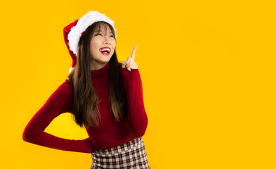 Young pretty asian woman in red sweatshirt wear santa hat finger pointing up yellow background. Merry Christmas theme.
