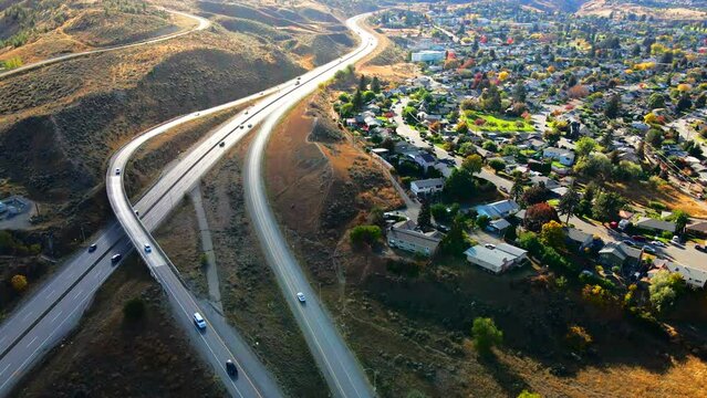 normal speed dolly in drone shot of Highway 1 in Kamloops BC Canada ,  with cars and trucks driving on the road, the city in the background in a desert environment on a sunny day