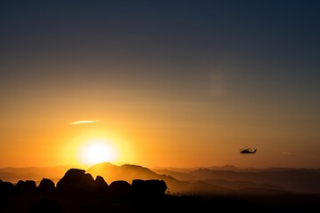 Fototapeta na wymiar Helicopter flying between mountains during orange sunset