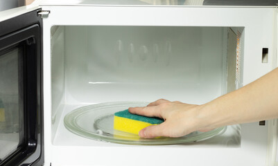 Close-up of female hand cleaning microwave oven with sponge. Concept of cleanliness and...
