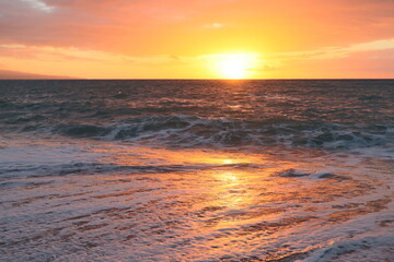 Sunset over a stormy sea. The orange sun on the horizon reflects on the surface of the water