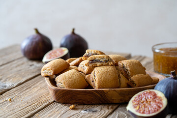 Biscuits filled with fig jam on wooden bowl, fresh figs, jam in jar on wooden background. Close up. 