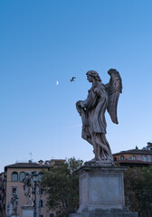 Statue of an angel with the moon in the background in the sky