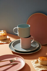 Pottery illustration. Lined up blue and pink ceramic plate and cup. Cake and fork on a pastel background.