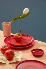 Red Ceramic dishes and tomatoes are placed on the table with tulip flowers in a vase. Red color ceramic kitchenware. Kitchen decoration.
