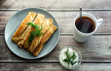 Pancakes with meat on a gray plate, sour cream, garnished with dill. Tea in a white cup. wooden background