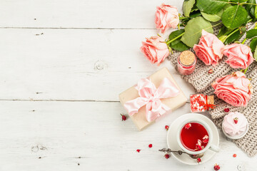 The concept of romantic tea. Wrapped gift, hibiscus tea, a bouquet of delicate roses, sweets