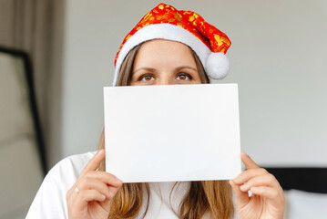 A girl is holding a blank letter to Santa Claus. Woman in a Christmas hat holding a letter in front...