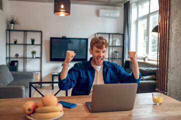 Man sitting in the home office at the laptop and looking excited