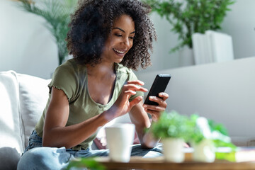 Shot of confident woman using her mobile phone while drinking coffee sitting on sofa at home.