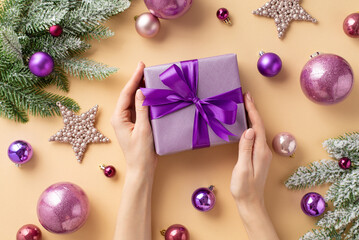 Christmas concept. First person top view photo of female hands holding lilac giftbox with purple...