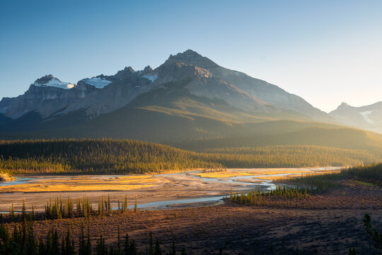 Mountain landscape at dawn. Sunbeams in a valley. Rivers and forest in a mountain valley at dawn. Natural landscape with bright sunshine. High rocky mountains. Banff National Park, Alberta, Canada.