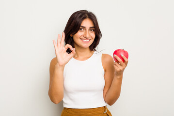 Young Indian woman holding an apple isolated on white background cheerful and confident showing ok...