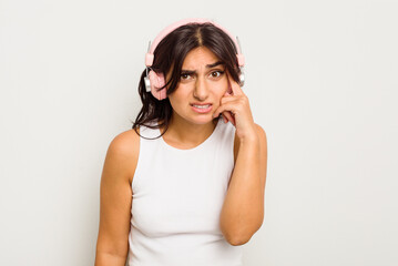 Young Indian woman wearing headphones isolated on white background showing a disappointment gesture with forefinger.