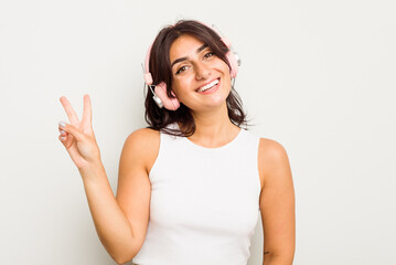 Young Indian woman wearing headphones isolated on white background joyful and carefree showing a peace symbol with fingers.