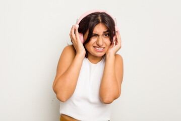 Young Indian woman wearing headphones isolated on white background covering ears with hands.
