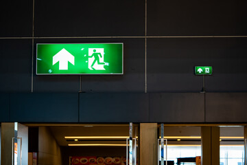 Big Emergency fire exit sign is placed on the black wall over the door of the exhibition hall.