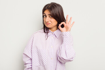Young Indian woman isolated on white background winks an eye and holds an okay gesture with hand.