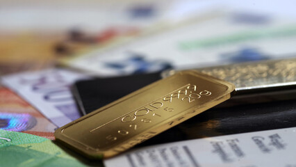 Minted gold bar weighing 20 grams against a blurred  background of euro banknote and certificate.