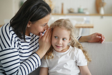 Mother telling secret, whispering to kid daughter, gossiping together at home. Trustful conversation