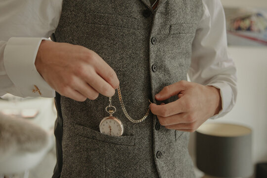 A groom dressed in a vintage-inspired vest, carefully holding a classic pocket watch, adding a timeless and elegant touch to his wedding attire.
