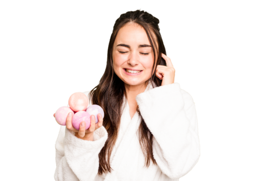 Young caucasian woman holding aromatic balls for bathtub isolated on green chroma background covering ears with hands.