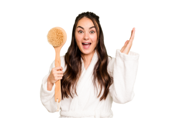 Young caucasian woman holding shower brush isolated on green chroma background receiving a pleasant surprise, excited and raising hands.