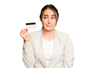 Young caucasian woman holding a credit card isolated on green chroma background confused, feels doubtful and unsure.