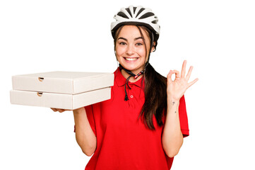 Young caucasian delivery woman holding a pizzas isolated on green chroma background cheerful and confident showing ok gesture.