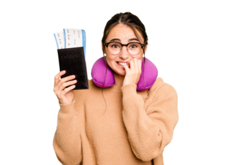 Young caucasian woman with inflatable travel pillow holding passport isolated on green chroma background biting fingernails, nervous and very anxious.
