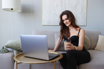 Young woman working at home on laptop and drinking coffee