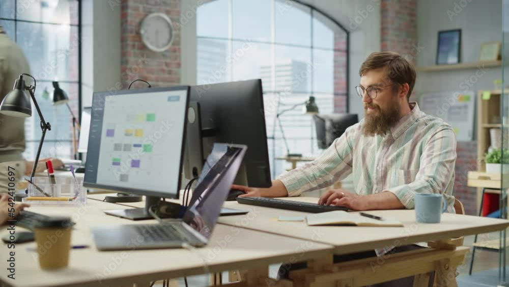 Poster Portrait of Creative Bearded White Man with Glasses Smiling While Using Computer in Bright Spacious Office. Male Team Manager Giving Feedback to colleagues. People Working in Background. Dolly Shot.
