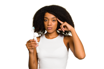 Young african american woman holding an electric toothbrush isolated pointing temple with finger, thinking, focused on a task.