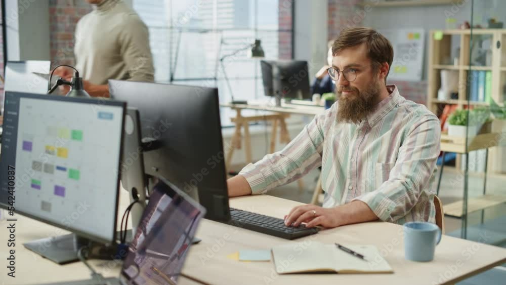 Poster portrait of young caucasian bearded man with glasses smiling while sitting and working on computer i