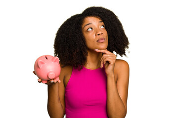 Young African American woman holding a piggy bank isolated looking sideways with doubtful and skeptical expression.